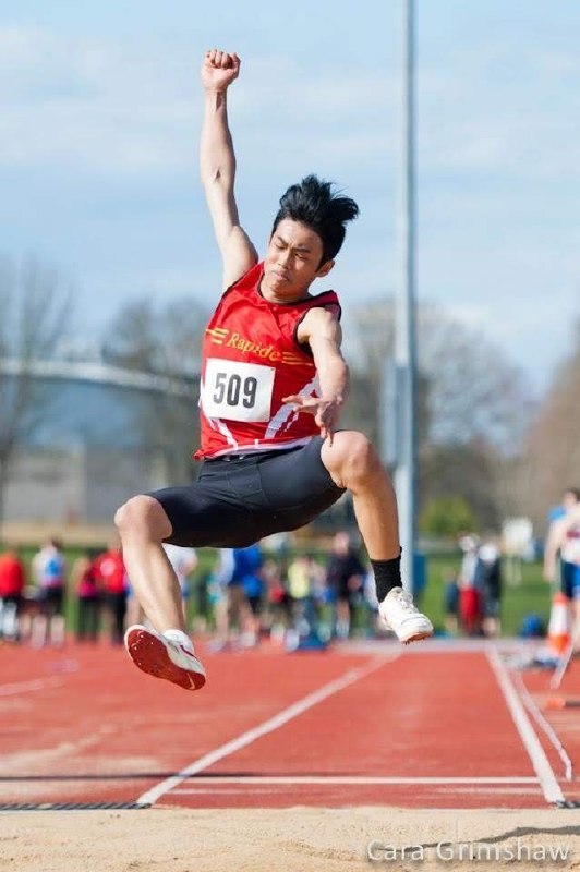 Club Rapide athlete landing a long jump, sand flying